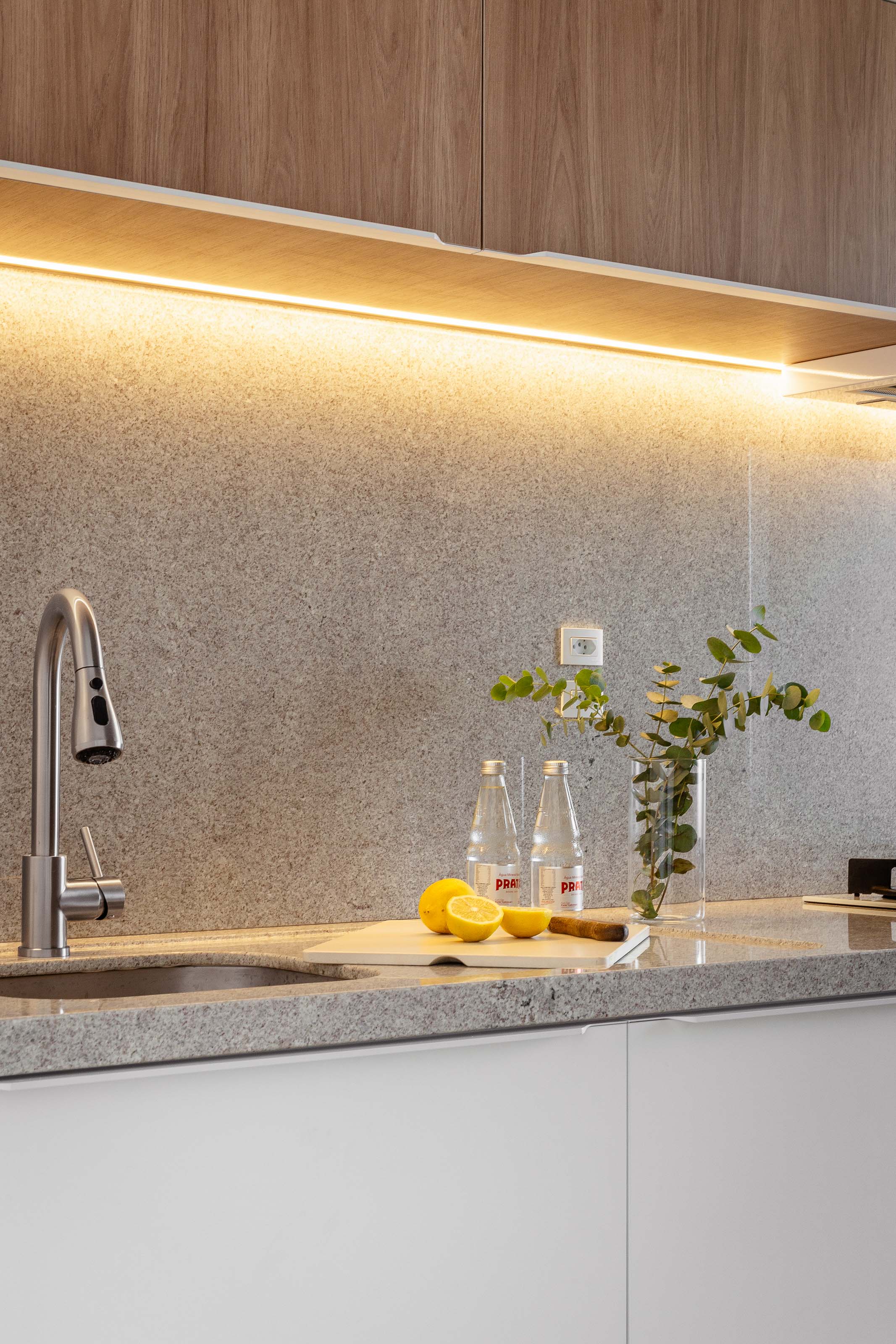 Cozinha com marcenaria amadeirada, bancada de pedra e iluminação baixa, projeto Clareira